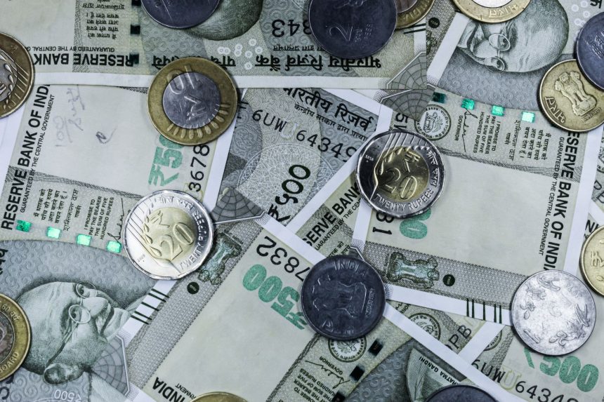 Notas de rupia indiana e moedas dispostas sobre uma superfície, representando o mercado financeiro do país
