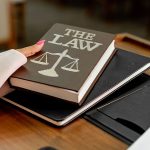 Livro com a inscrição “The Law” ao lado de uma balança da justiça sobre uma mesa de madeira.