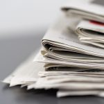Jornais empilhados sobre uma mesa, representando a imprensa e o jornalismo.