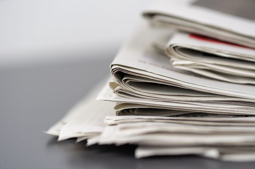 Jornais empilhados sobre uma mesa, representando a imprensa e o jornalismo.