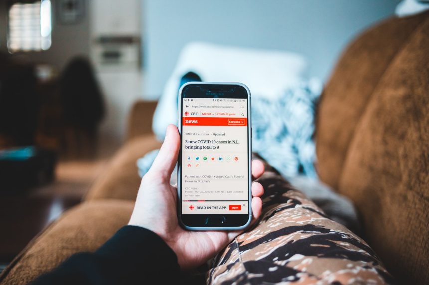 Pessoa lendo notícias em um smartphone enquanto relaxa em um sofá.