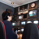 Profissional trabalha em uma sala de controle de TV com várias telas e equipamentos de transmissão.