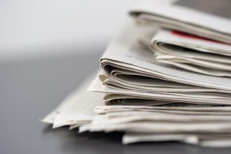 Jornais empilhados sobre uma mesa, representando a imprensa escrita e o trabalho editorial.