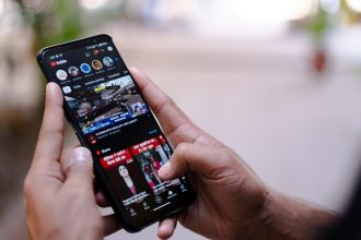 Mãos seguram um smartphone exibindo um vídeo ao ar livre.
