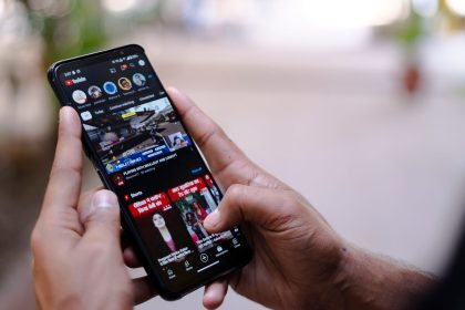 Mãos seguram um smartphone exibindo um vídeo ao ar livre.