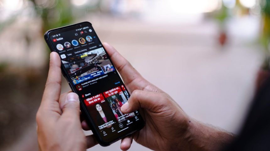 Mãos seguram um smartphone exibindo um vídeo ao ar livre.
