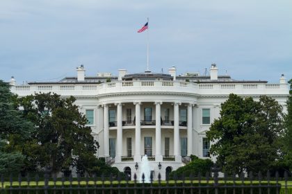 Vista frontal da Casa Branca, com a bandeira dos Estados Unidos e vegetação ao redor