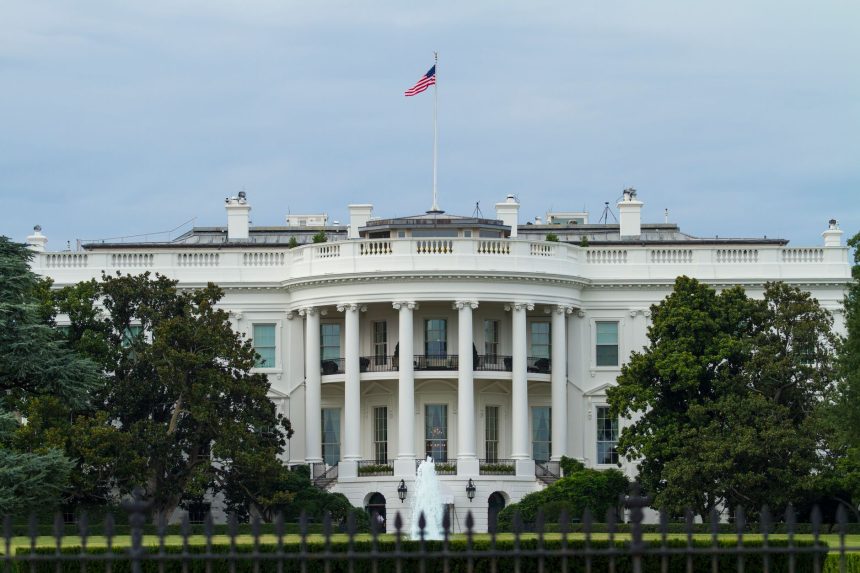 Vista frontal da Casa Branca, com a bandeira dos Estados Unidos e vegetação ao redor