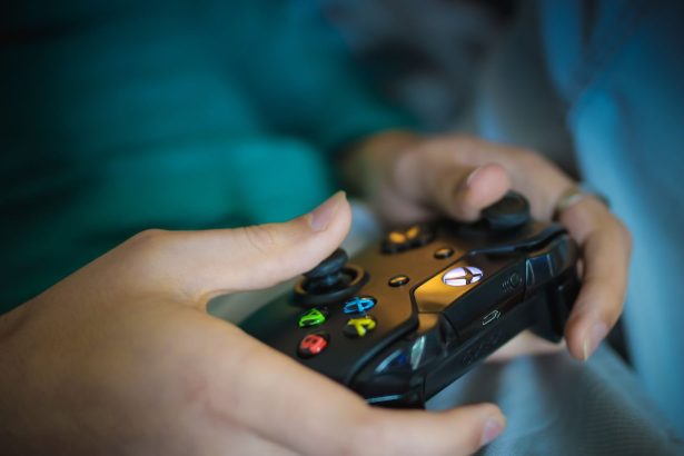 Mãos seguram um controle sem fio moderno de videogame em ambiente interno.