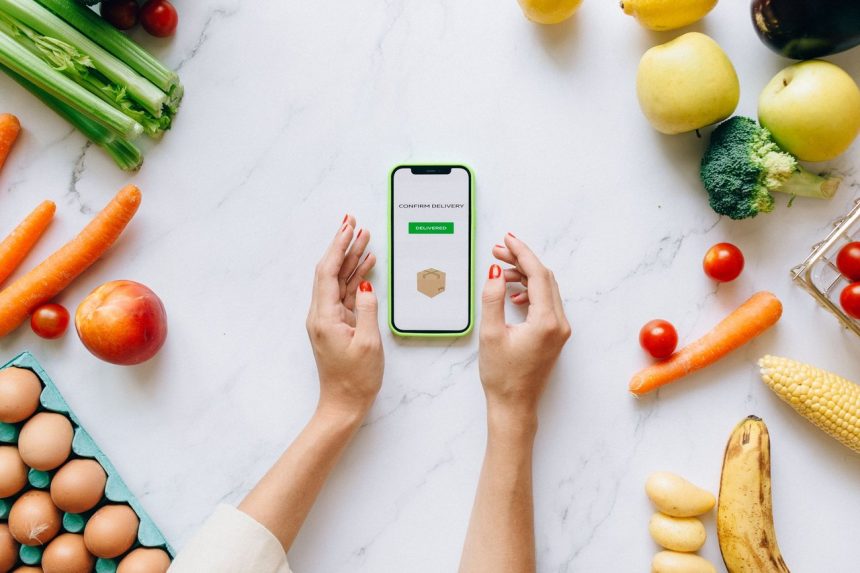 Mãos seguram um celular sobre uma bancada com frutas e verduras frescas.
