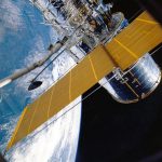 Espaçonave com painéis solares orbitando a Terra, vista contra o fundo escuro do espaço.